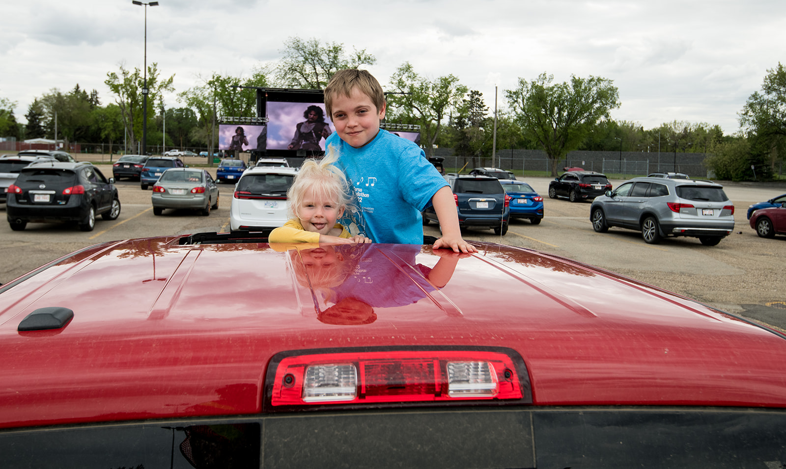 kids peeking out of sunroof in parking lot at outdoor movie event