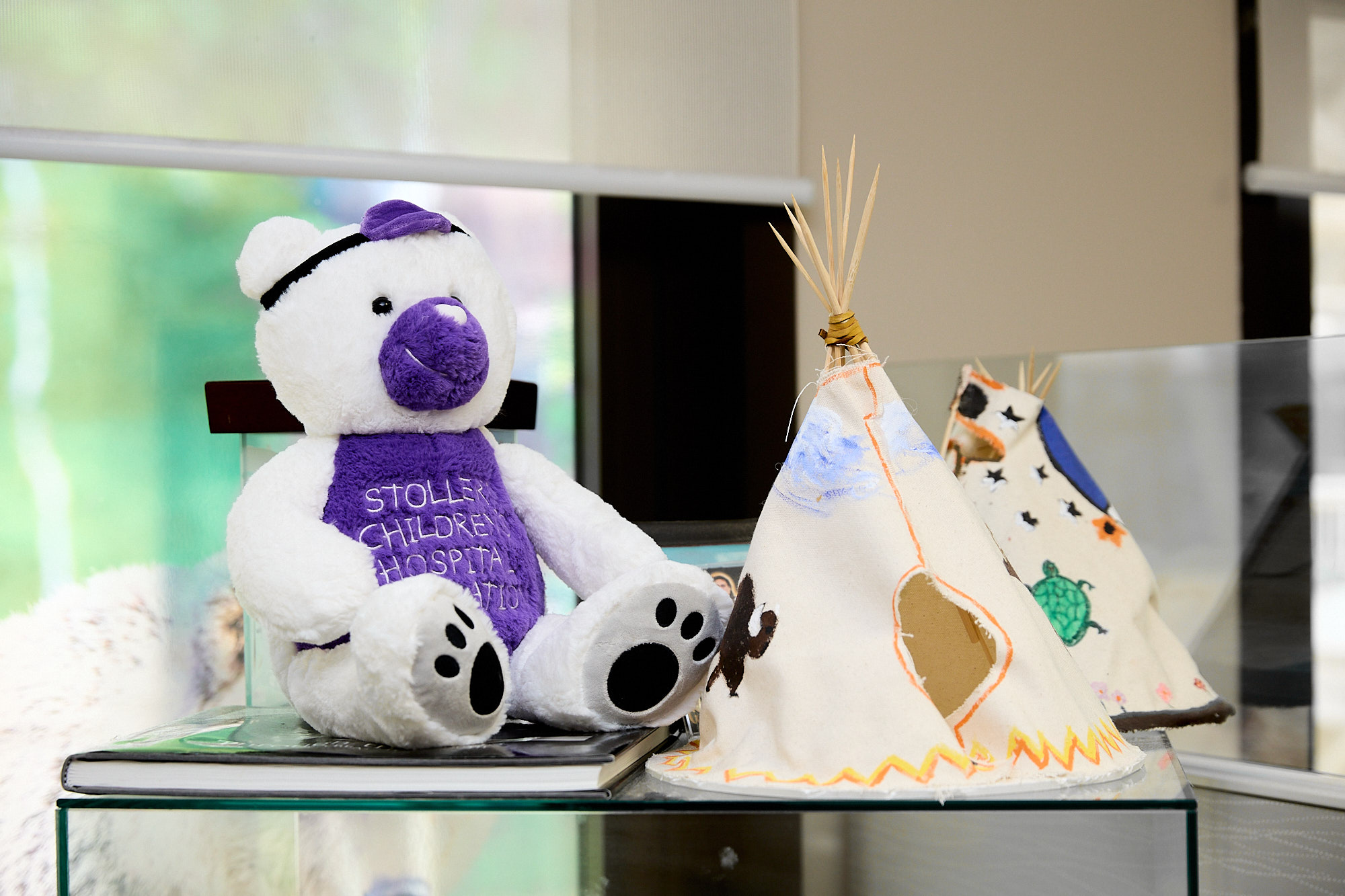 Stollery white and purple bear stuffy sitting on a shelf with two tipis.