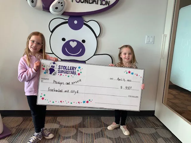 two girls holding giant cheque in stollery foundation office
